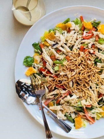 asian chicken salad on a white plate with serving utensils