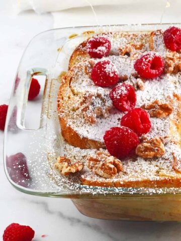 French toast casserole in glass baking dish with powdered sugar and berries on top.