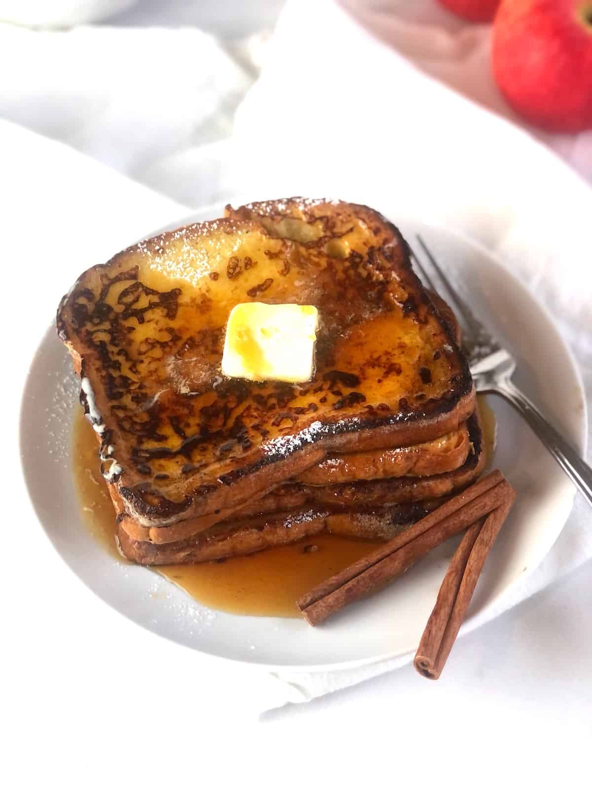 A plate of apple cider french toast with butter and cinnamon.