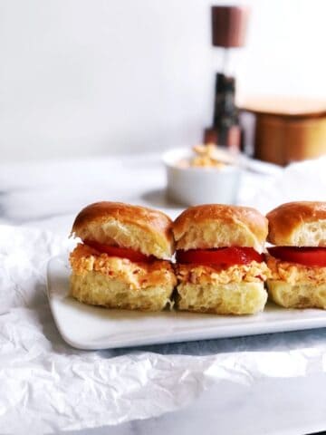 Pimento cheese sandwiches on a white plate with tomatoes.