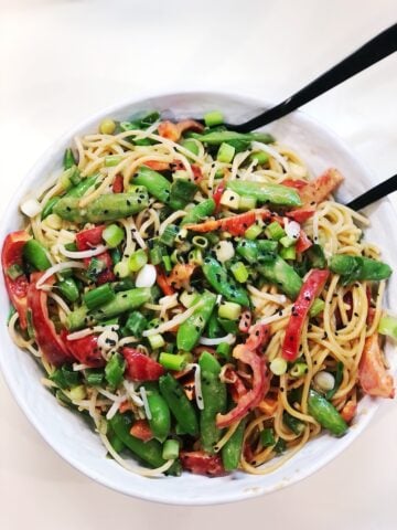 peanut pasta veggie salad in white bowl with serving spoon